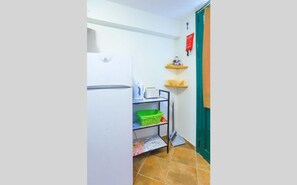 A compact kitchen with a white refrigerator, a small shelf with a kettle and toaster, and a green basket on a shelf. - Agapi Studio in Kalami (Kalami)