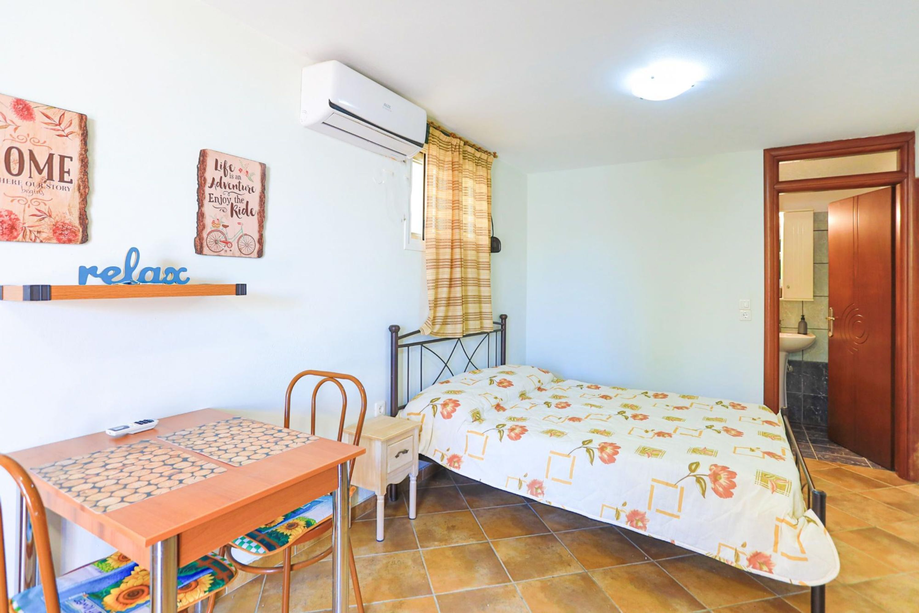 A bedroom with a bed, a desk with a chair, a small table, and a window with curtains.