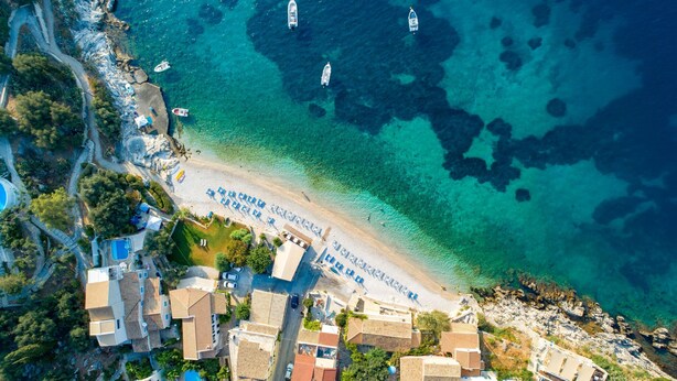 An aerial view of a coastal town with clear turquoise waters, boats, and a beach with a sign. - Takis House in Katavolos (Katavolos)