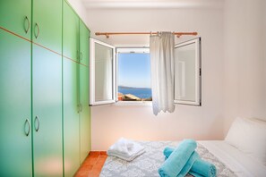 A bedroom with a bed, green wardrobe, and a window with a view of the sea. - Takis House in Katavolos (Katavolos)