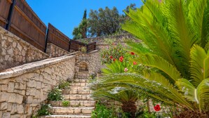 A stone staircase leading up to a wooden fence, surrounded by lush greenery and flowering plants. - Takis House in Katavolos (Katavolos)
