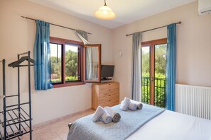 Ein Schlafzimmer mit einem Bett, einem Fernseher auf einer Holzkommode, einem Wäscheständer und einem Balkon mit Vorhängen.