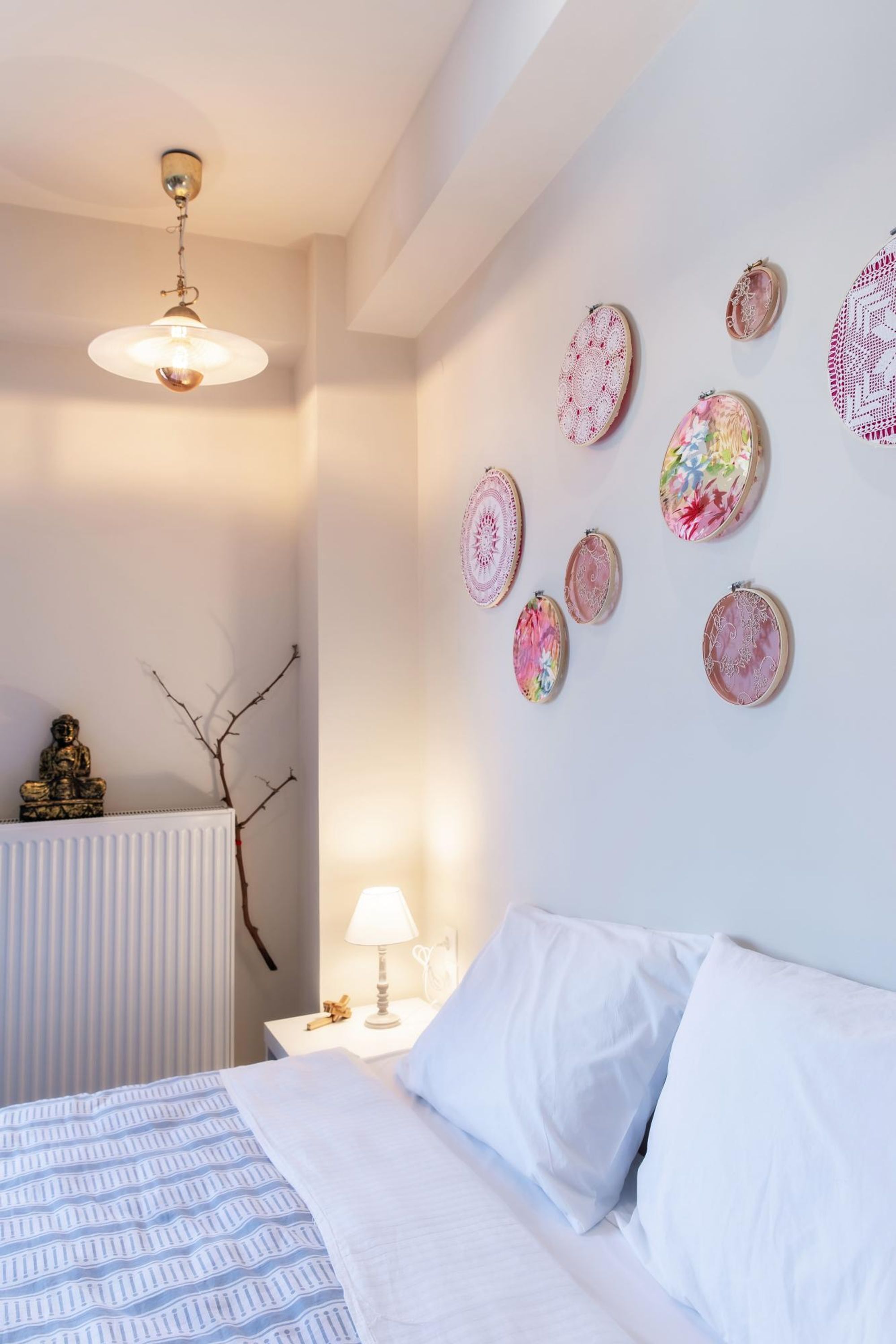 Un dormitorio con cama, ropa de cama blanca, una lámpara de noche y adornos en la pared.