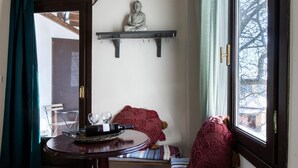 Una stanza accogliente con pavimento in legno, un tavolo rotondo con un vassoio, una panca con una coperta e una finestra vista alberi.