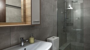 Un bagno moderno con un lavandino bianco, uno specchio, un water e una doccia vetrata.
