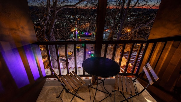 A balcony with a table and chairs, a stone floor, and a view of a cityscape at dusk. - Stagiates Guest House Room 3 (Μακρινίτσα)