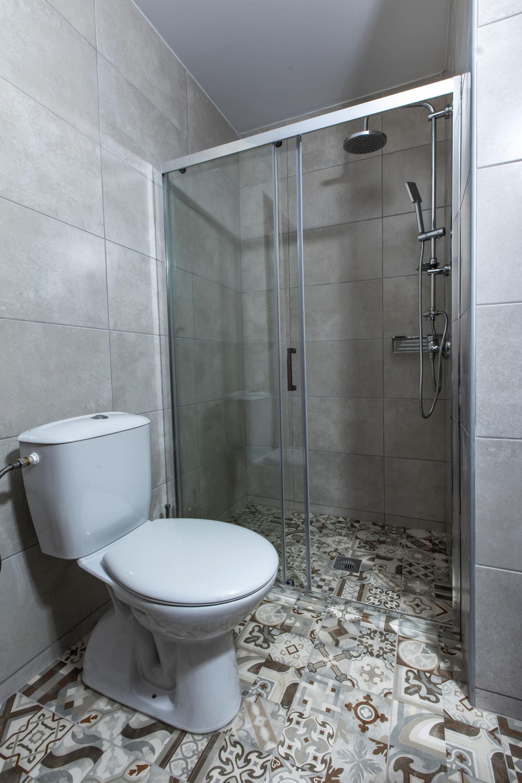 A bathroom with a toilet, a shower enclosure, and patterned floor tiles.