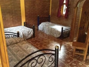 A room with two beds, a wooden door, and a brick wall. - Centro Ecoturístico Shambala (Zitácuaro)