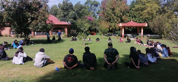 A group of people sitting on grass in a park-like setting with buildings in the background. - Centro Ecoturístico Shambala (Zitácuaro)