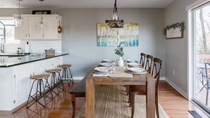 Cozinha moderna com armários brancos, uma mesa de jantar de madeira para seis pessoas, e uma janela grande que ilumina naturalmente o espaço.