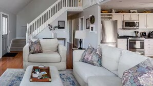 Uma sala de estar ampla com uma escada branca, uma cozinha com armários brancos e uma área de refeições.