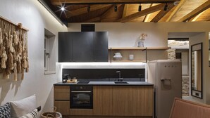Une cuisine compacte équipée d’un four encastré, d’un évier et d  ’un réfrigérateur. Le plafond est en bois et un mur en pierre se trouve au fond.