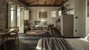 Une pièce rustique avec des poutres apparentes, un mur en pierre, un canapé, une table à manger et un coin cuisine.