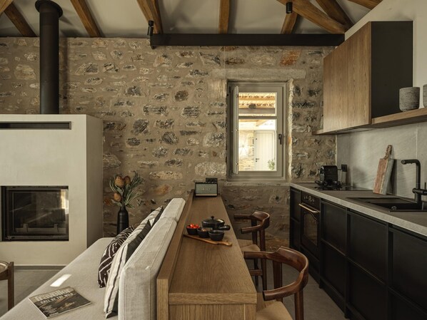 Una cocina con pared de piedra, vigas de madera, estufa integrada y una ventana.