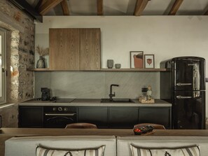 Une cuisine moderne avec un mur en pierre, des meubles en bois, un réfrigérateur noir et un coin repas avec deux canapés.