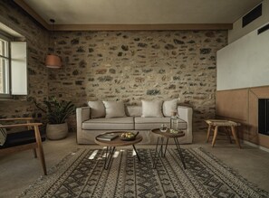 Un salon chaleureux avec un mur en pierre, un canapé, une table basse, une table d’appoint, une plante en pot et un tabouret en osier.