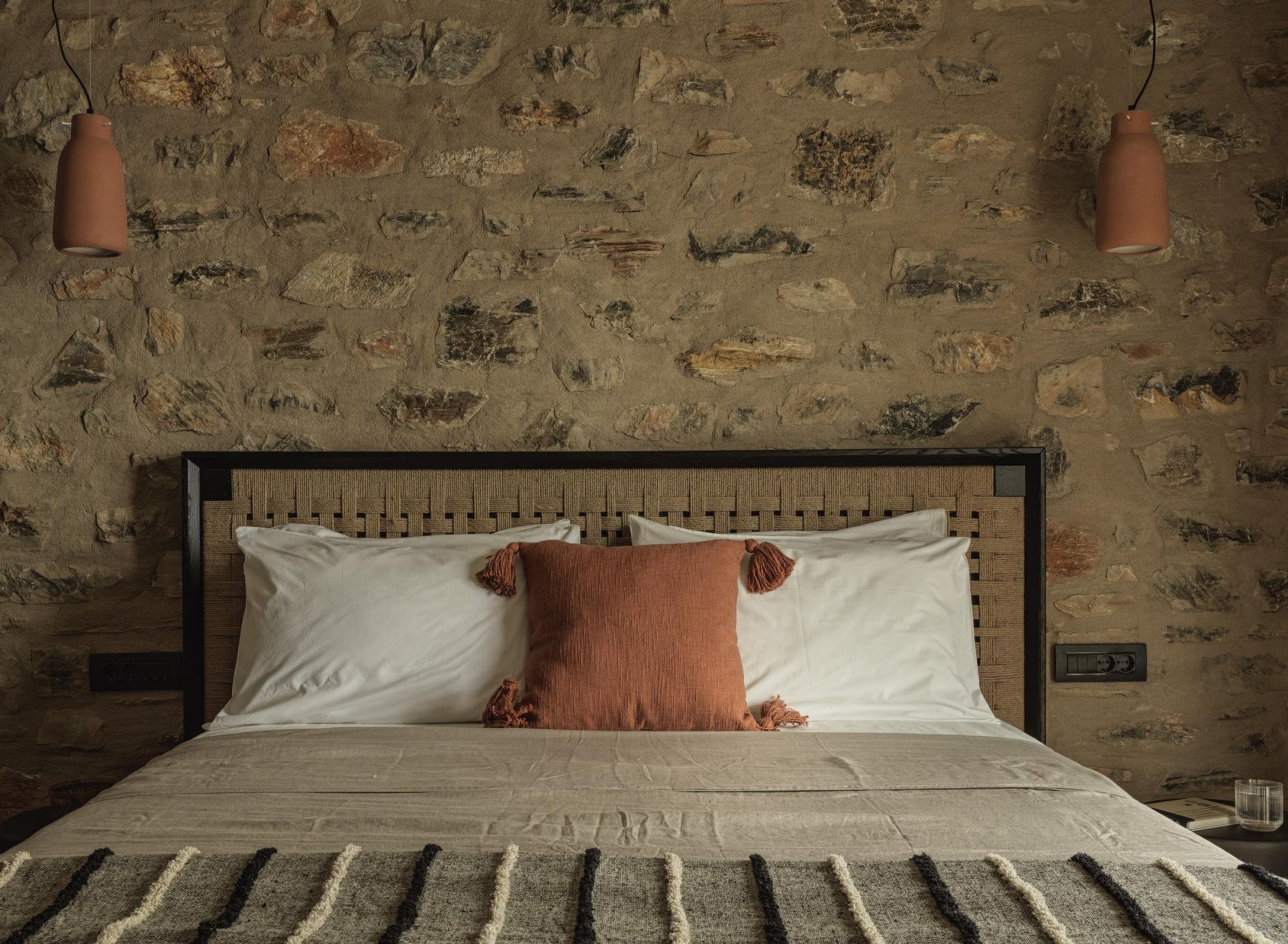 A bed with a woven headboard, two white pillows, and a brown throw pillow.