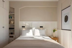 A neatly arranged bedroom with a large bed, built-in shelving, a bedside table with a vase, and a framed picture on the wall. - Meliti Apartment in Plaka (Athina)