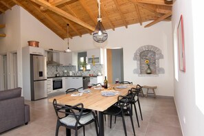 A modern kitchen with a wooden ceiling, a dining area with a wooden table and chairs, and a stone fireplace. - Irini Villa by Elrin Villas Mani (Neochori)