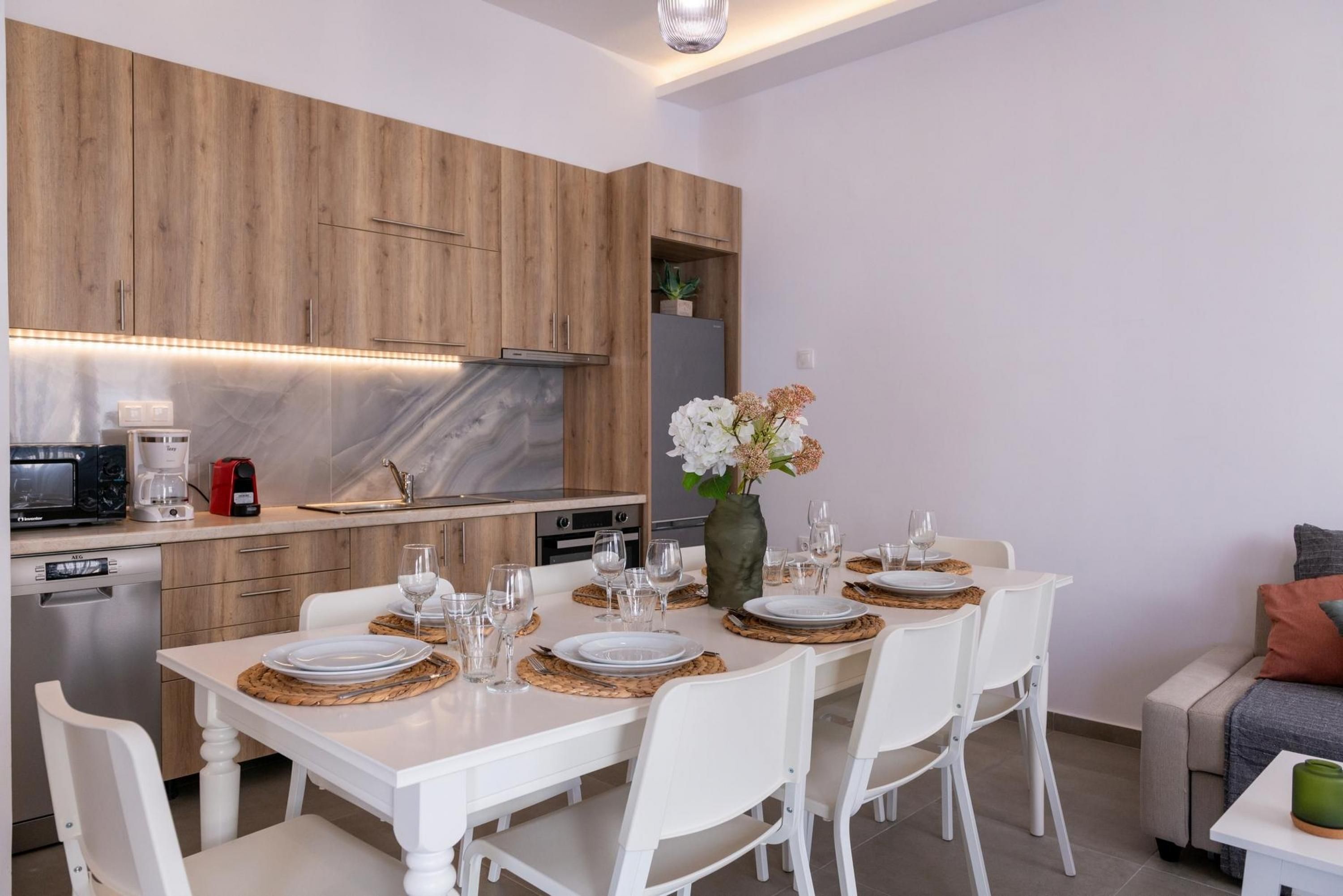 Eine moderne Küche mit Holzschränken, einer Marmorarbeitsplatte und einem Essbereich für vier Personen mit weißen Stühlen und einem Blumenstrauß.