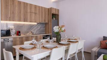 Eine moderne Küche mit Holzschränken, einer Marmorarbeitsplatte und einem Essbereich für vier Personen mit weißen Stühlen und einem Blumenstrauß.
