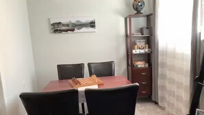 Un área de comedor con una mesa de madera y sillas negras, una estantería con libros y objetos decorativos, y un cuadro en la pared.