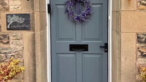 Una puerta gris con un adorno morado, un buzón y una placa de piedra que dice "Lower Abbey Mill House".