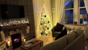 Un salón acogedor con chimenea, televisor montado en la pared, un árbol de Navidad y un sofá confortable.