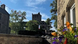 Un patio con un muro de piedra, un pequeño puente y un edificio con una torre al fondo.