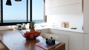 Eine Küche mit einer Holztresen, einer Obstschale, einer Vintage-Kamera und Blick auf das Meer durch ein großes Fenster.