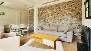 Ein modernes Wohnzimmer mit grauem Sofa, weißen Sesseln, einem Holztisch und einer Steinwand.