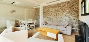 A modern living room with a grey sofa, white chairs, a wooden coffee table, and a stone wall. - Dizengoff Brique in Tel Aviv-Yafo (Tel Aviv-Yafo)
