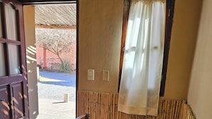 Une pièce avec une table en bois, un banc, une fenêtre avec un rideau et une porte donnant sur l’extérieur.