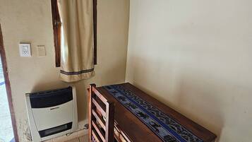 A small room with a wooden table and a chair, a window with a curtain, and a wall-mounted heater.