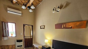 Une chambre à coucher comprenant un lit, un banc, une table de chevet avec une lampe, une étagère fixée au mur et une fenêtre avec des rideaux.