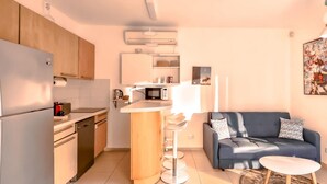 A compact kitchen with modern appliances, a central island, and a dark blue sofa with a small table. - Dizengoff Muguet in Tel Aviv-Yafo (Tel Aviv-Yafo)