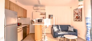 Eine kompakte Küche mit modernen Geräten, einer zentralen Kücheninsel und einem dunkelblauen Sofa mit kleinem Tisch.