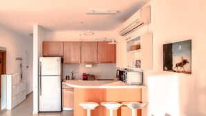 A modern kitchen with wooden cabinets, a refrigerator, a microwave, and a sink. There are three white bar stools at the counter. - Dizengoff Muguet in Tel Aviv-Yafo (Tel Aviv-Yafo)