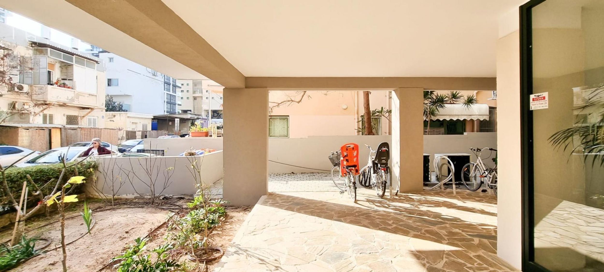Un espacio al aire libre techado con piso de piedra, bicicletas y un coche estacionado cerca.