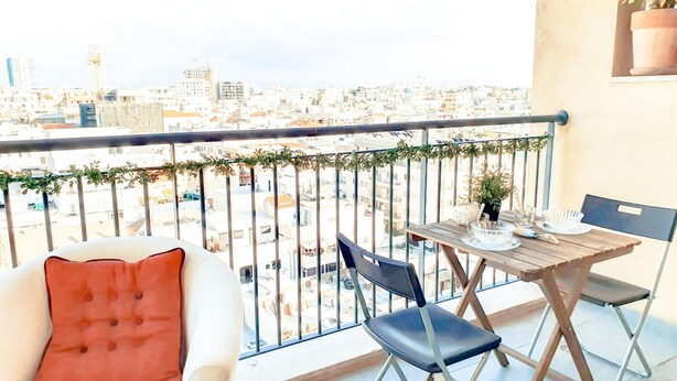 Ein Balkon mit Blick auf eine Stadtlandschaft, einem Tisch mit Stühlen und einem Blumentopf.