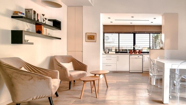 A modern living room with a sofa, armchair, and coffee table, leading to a kitchen with a dining area. - Rupin Nacre in Tel Aviv-Yafo (Tel Aviv-Yafo)
