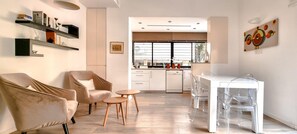 Een moderne woonkamer met een bank, fauteuil en salontafel, die uitkomt op een keuken met een eethoek.