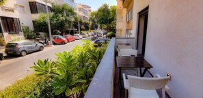 Ein Balkon mit Gartenmöbeln, Blick auf eine belebte Straße mit parkenden Autos und Gebäuden im Hintergrund.
