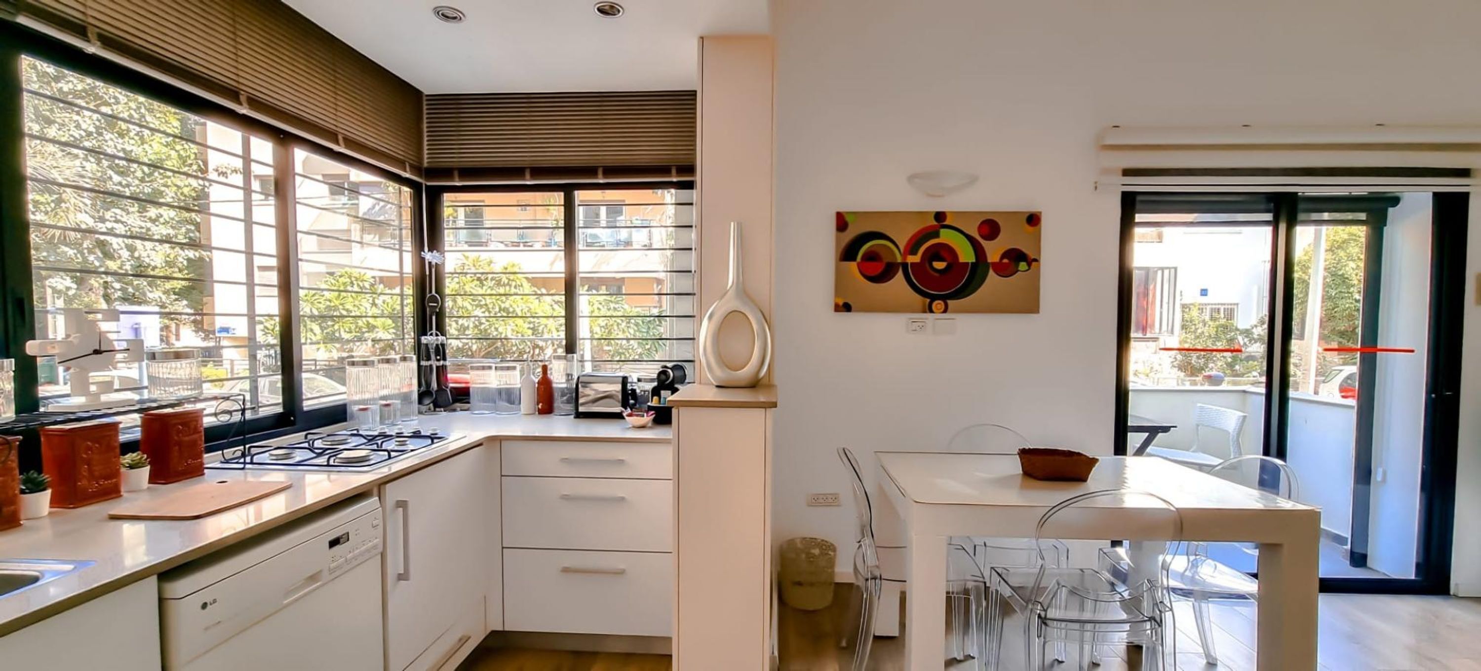 A modern kitchen with a gas stove, white cabinets, and a dining area with clear chairs.