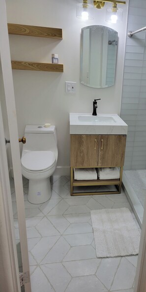 Une salle de bain comprenant des toilettes, un lavabo, un meuble en bois, un miroir et un sol carrelé.