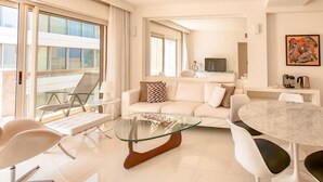 A modern living room with a glass coffee table, white sofas, a dining table, and a TV. - Ramat Yam Marine in Herzliya (Tel Aviv-Yafo)