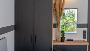 Una habitación moderna con un armario de madera oscura, un escritorio de madera con una planta en maceta, helechos de pampa y un control remoto.