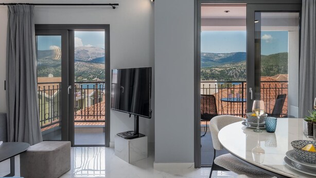 Una habitación de hotel moderna con balcón, televisor de pantalla plana, zona de comedor con mesa y sillas, y vistas a las montañas.