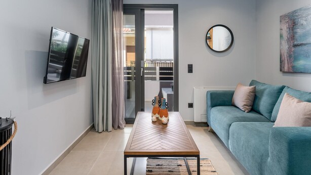 Una sala de estar moderna con un sofá, una mesa de centro, un televisor y un ventanal corredera que da a un balcón.