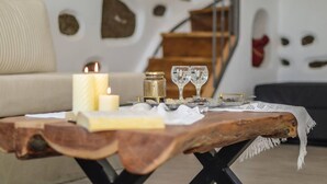 Uma mesa de centro de madeira com velas, copos e um pote. Um sofá e uma escada estão ao fundo.